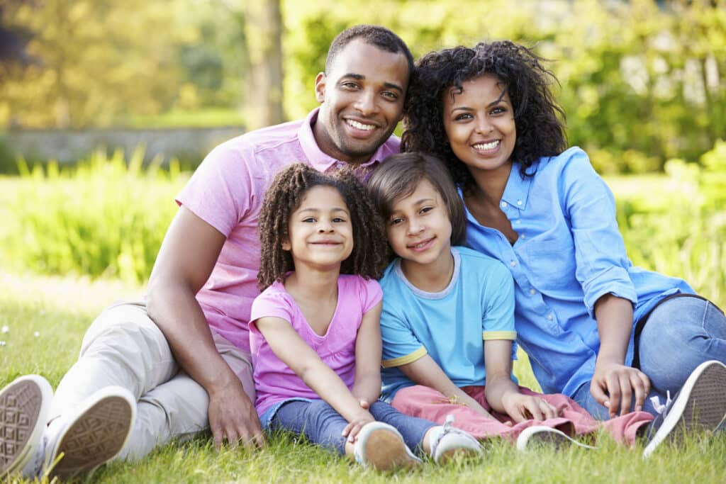 Cosmetic Dentistry - African American Family Sitting In Garden Smiling At Camera
